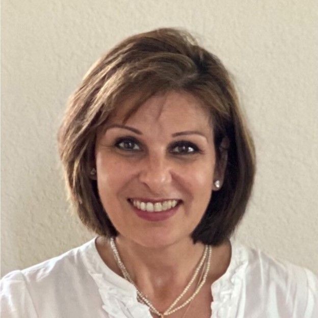 Woman wearing a white blouse and pearl necklace against a plain background.