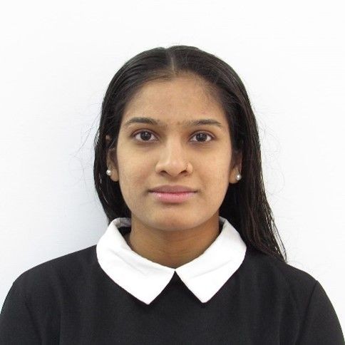 Person wearing a black top with a white collar and pearl earrings against a plain white background.